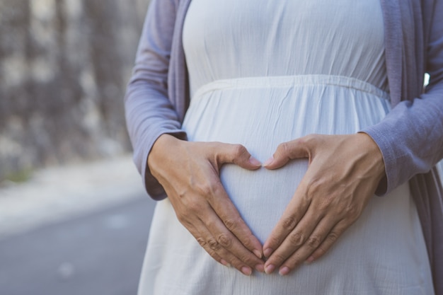 Forma de coração na barriga de grávida. fundo ao ar livre