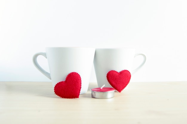 Forma de coração vermelho com duas canecas brancas na mesa de madeira
