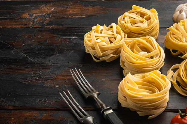 Forma de tagliatelle enrolada de massa italiana com conjunto de ingredientes, em uma velha mesa de madeira escura