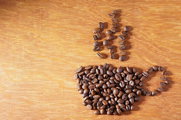 Foto forma de xícara de café de grãos de café torrados no fundo de madeira