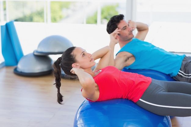 Forma pareja joven haciendo ejercicio en pelotas de fitness en el gimnasio