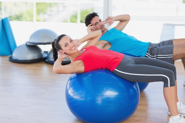 Forma pareja joven haciendo ejercicio en pelotas de fitness en el gimnasio