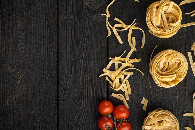 Forma de tallarines enrollados de pasta italiana con conjunto de ingredientes, sobre mesa de madera negra, vista superior plana