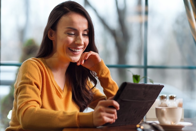 Forma de trabajo. Feliz mujer alegre alegre mirando la pantalla mientras sonríe y usa la tableta