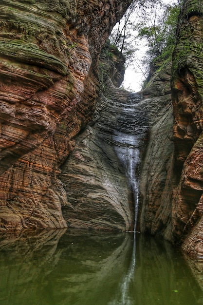 Foto formação rochosa no meio de árvores com pequena cachoeira