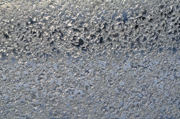 Formación de hielo en el cristal de la ventana, escarcha sobre fondo de cielo azul en invierno