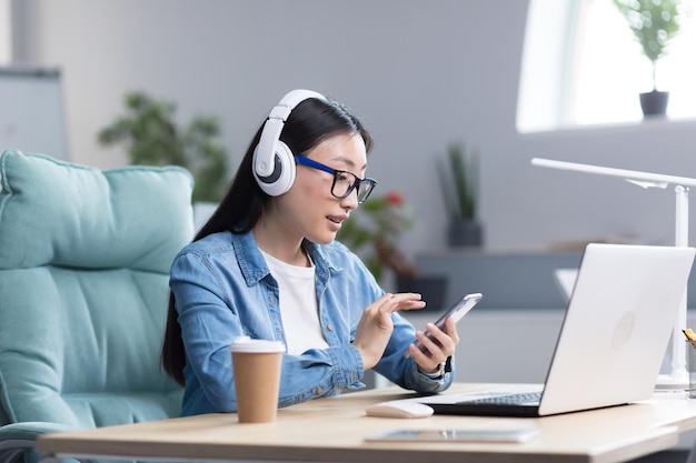 La formación en línea de una joven y hermosa estudiante asiática con anteojos está estudiando en una laptop en