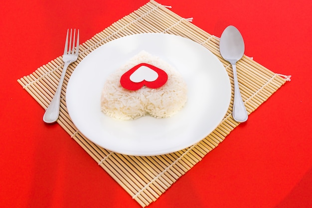 Formas de corazón de arroz cocido con una cuchara y un tenedor en un plato blanco