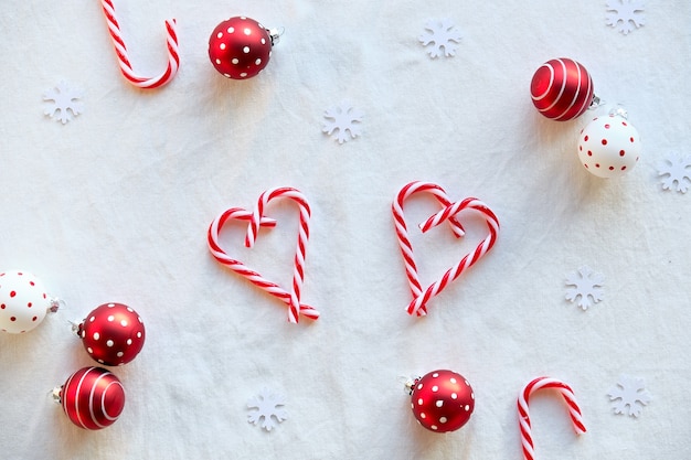 Formas de corazón hechas de bastones de caramelo, baratijas manchadas de blanco rojo sobre textil blanco.