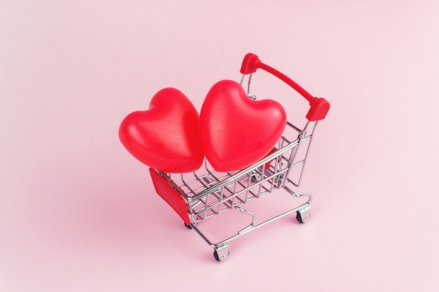 Formas de coração vermelho no mini carrinho de compras no conceito de fundo, compras e amor rosa.
