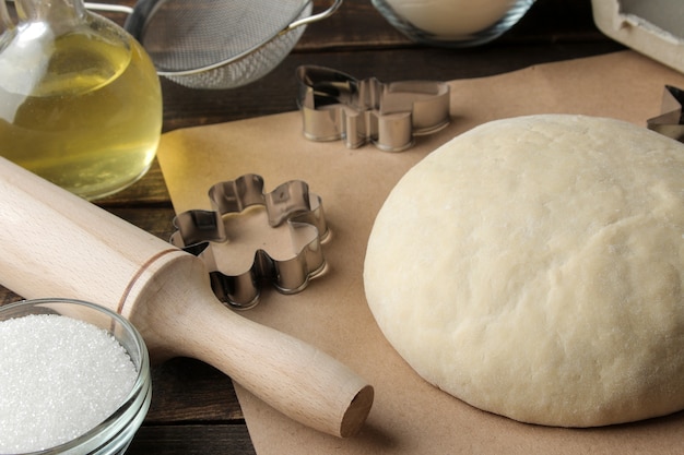 Formas de galletas de masa e ingredientes para hornear y herramientas para hornear en una mesa de madera marrón.