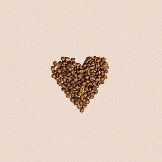 Formen Sie ein Herz aus Kaffeebohnen auf beigem Hintergrund. Liebeskaffeekonzept, braun geröstet