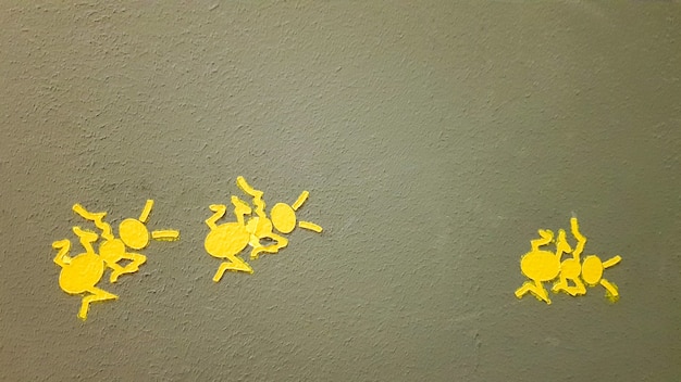 Formiga pintada de amarelo em uma parede cinza. formiga escalando uma parede. planos de fundo coloridos de formigas. artistas locais decoram as paredes das ruas.