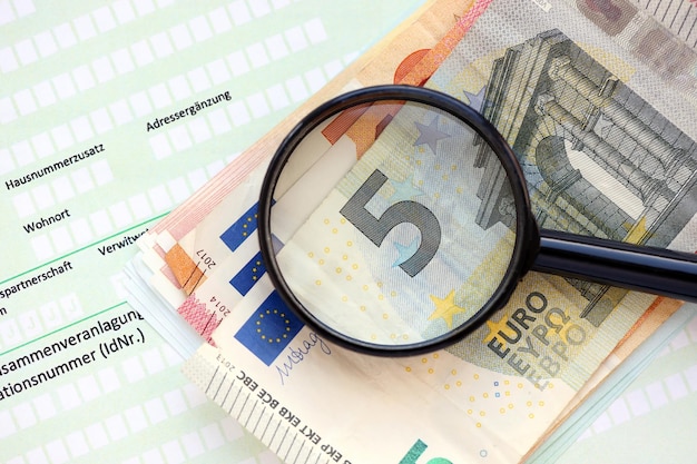 Formulário de declaração de imposto de renda alemão com lupa e notas de dinheiro europeias em euro encontra-se na mesa do contador de perto Contribuintes na Alemanha usando moeda euro para pagar impostos