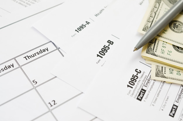 Formulario IRS 1095-A 1095-B y 1095-C en blanco se encuentra en la página de calendario vacía con bolígrafo y billetes de dólar