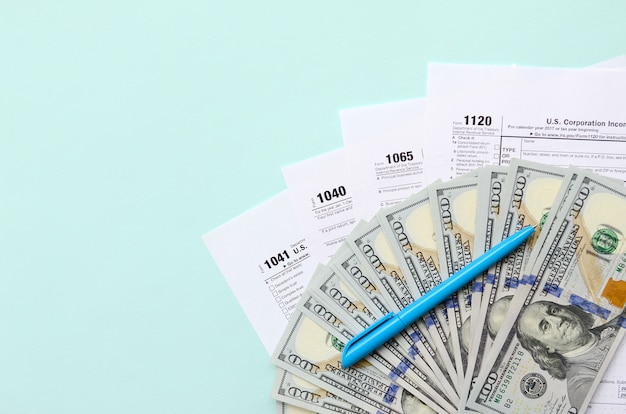 Formularios de impuestos se encuentra cerca de billetes de cien dólares y pluma azul