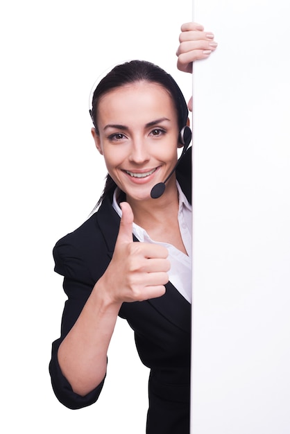 Fornecendo apenas suporte de qualidade. mulher jovem e bonita com fone de ouvido em pé perto do espaço da cópia e sorrindo enquanto isolada no branco