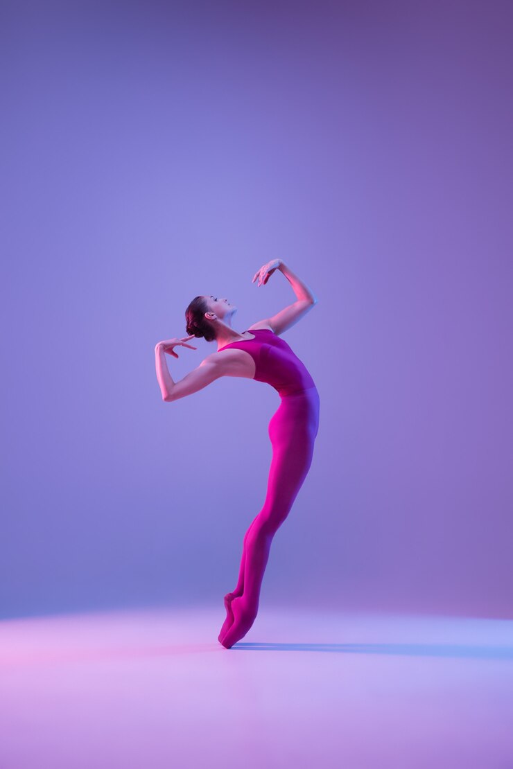 Foto forte. dançarina de balé jovem e graciosa isolada no fundo roxo do estúdio em luz de néon. arte, movimento, ação, flexibilidade, conceito de inspiração. dançarina de balé caucasiana flexível, saltos sem peso.
