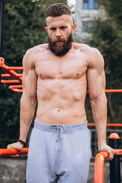 Forte homem barbudo musculoso fazendo flexões em barras assimétricas no ginásio de rua ao ar livre. Conceito de estilo de vida de treino.