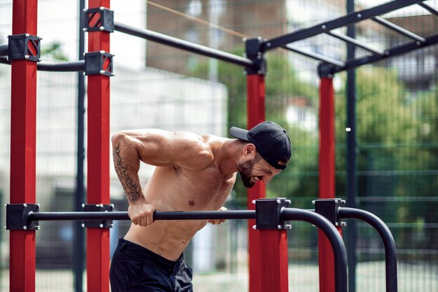 Forte homem musculoso fazendo flexões em barras assimétricas no ginásio de rua ao ar livre