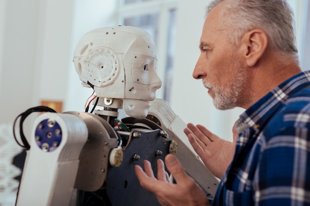 Fortschrittliche Technologie. Ernsthafter kluger Ingenieur, der den Roboter betrachtet, während er vor ihm steht