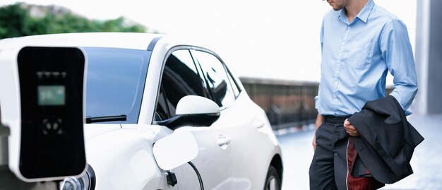 Fortschrittlicher Geschäftsmann mit EV-Auto an der Ladestation für öffentliche Parkplätze