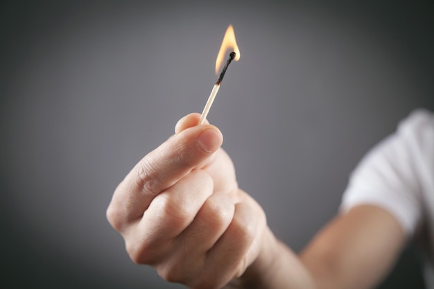 Fósforo ardiendo en mano masculina en fondo gris.