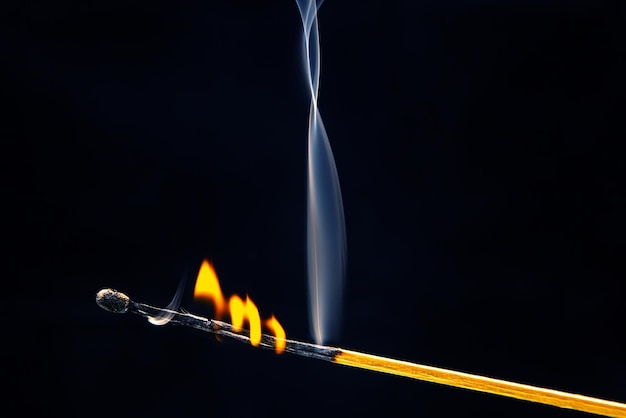 Foto fósforo de madeira piscando e queimando em um fundo escuro fechado fogo brilhante e fumaça de uma árvore em chamas