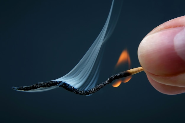 Fósforo de madera ardiendo y fumando en la mano sobre fondo oscuro. fuente de fuego