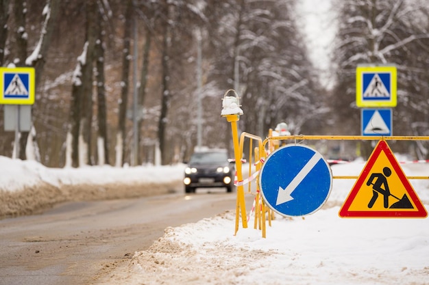 Un foso en una carretera de invierno con una valla y señales de advertencia y coches que pasan al fondo