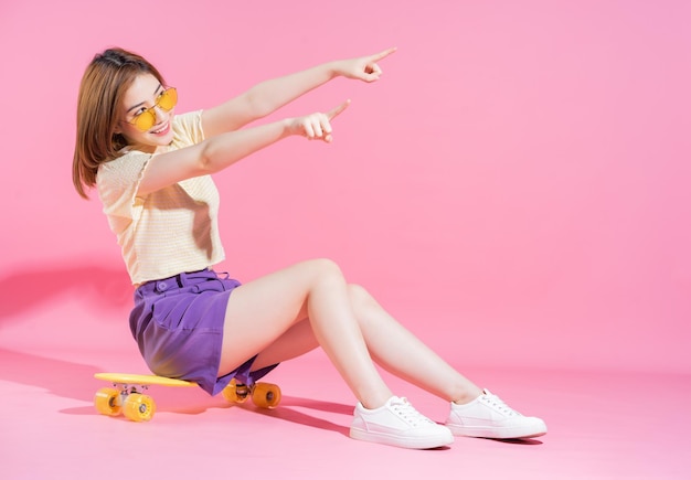 Foto de una adolescente asiática con monopatín sobre fondo rosa