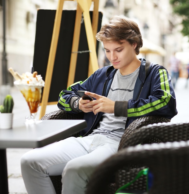 Foto de un adolescente leyendo un texto mientras está sentado en un café al aire libre
