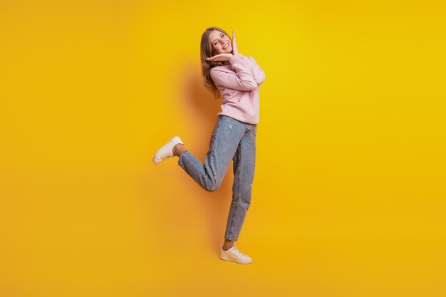 Foto de adorable niña alegre soporte una pierna palmas cara sobre fondo amarillo