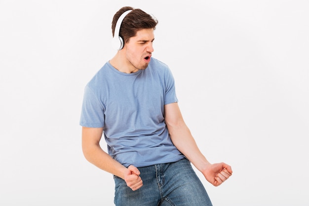 Foto de un adulto sonriente con cabello corto y oscuro escuchando música a través de auriculares y expresando placer en la cara, aislado sobre la pared blanca