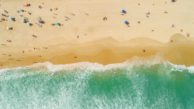 Foto aérea bloqueada de ondas quebrando na praia. guarda-chuvas de praia coloridos e pessoas aproveitando o verão.