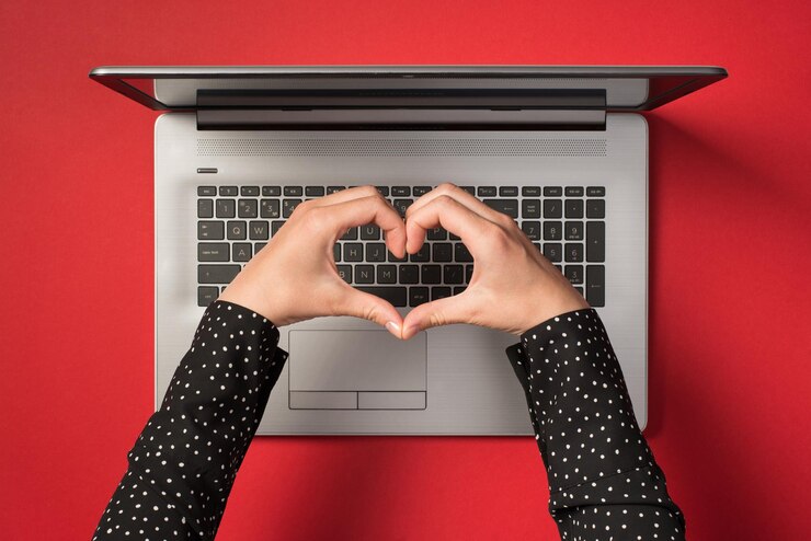 Foto foto aérea de una computadora portátil gris y manos con un gesto como corazón aislado en el fondo rojo