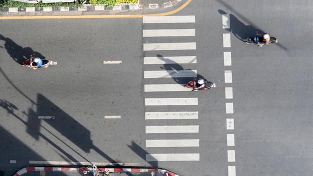 Foto aérea da vista superior da motocicleta que conduz a faixa de travessia pedestre da passagem na estrada do tráfego com a silhueta da luz e da sombra.