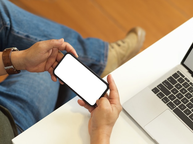 Foto aérea de freelancer masculino segurando um smartphone com tela horizontal na área de trabalho