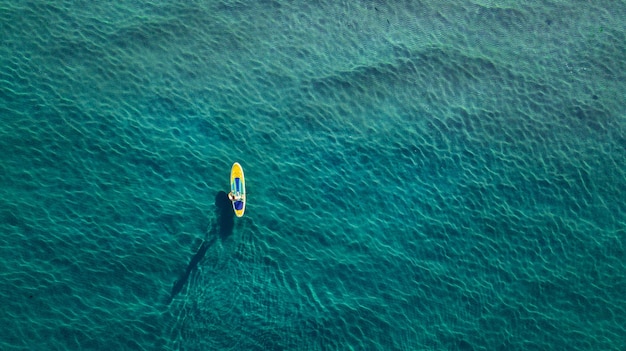 Foto aérea de homem a bordo de supino em um mar azul claro