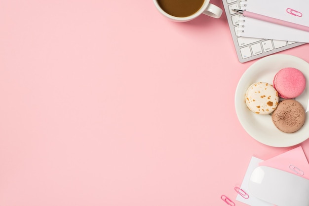 Foto aérea de teclado computador mouse xícara de café com clipes de papel de caneta e placa de vários biscoitos isolados no pano de fundo rosa com copyspace