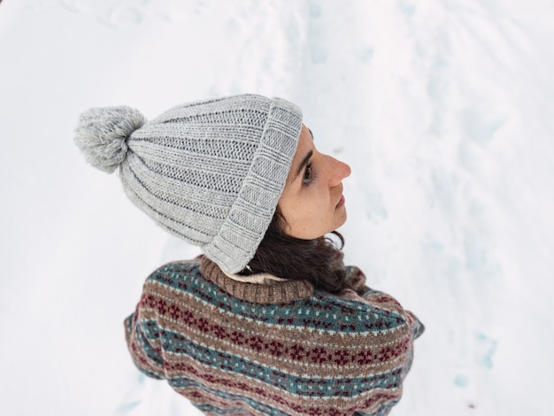 Foto aérea de uma linda jovem na neve vestida com roupas de inverno