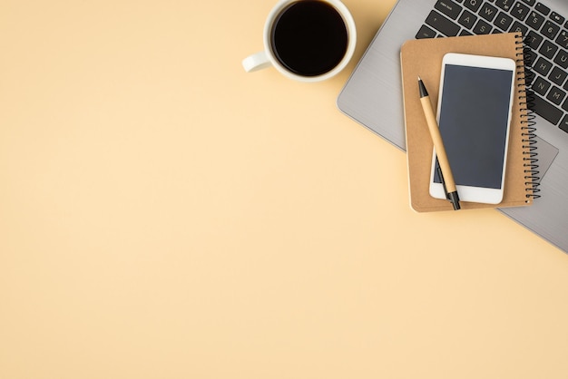 Foto aérea do bloco de notas da xícara de café do laptop cinza com caneta e telefone isolado no pano de fundo bege com espaço em branco