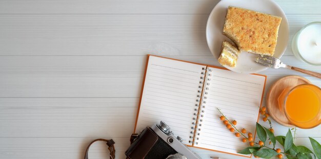 Foto aérea do espaço de trabalho acolhedor com o caderno em branco com torradas de pão e um copo de suco de laranja