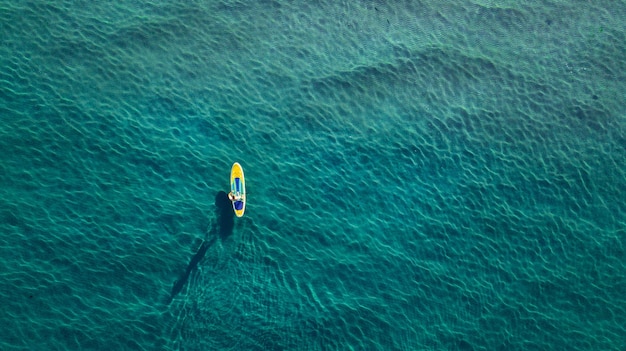 Foto aérea del hombre a bordo de sup en mar azul claro