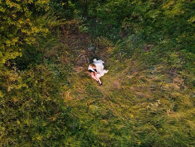 Foto aérea de una mujer rubia sentada en el césped y jugando con su perro