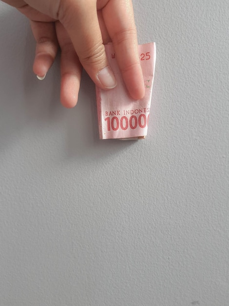 Foto aislada de una mano que sostiene un billete de cien mil rupias