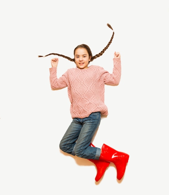 Foto foto aislada de la parte superior de la niña feliz saltando en botas de goma rojas