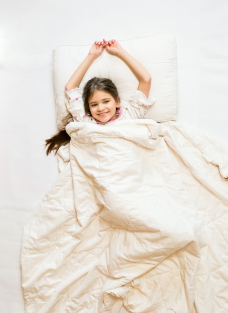 Foto aislada desde el punto más alto de la niña sonriente acostada en la cama