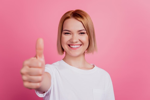 Foto de la alegre dama promotora positiva levantar el pulgar hacia arriba aprobar la elección usar camiseta blanca aislada sobre fondo rosa