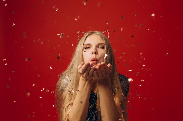 Foto de una alegre y encantadora chica hermosa que sopla confeti de sus manos aislada de fondo rojo